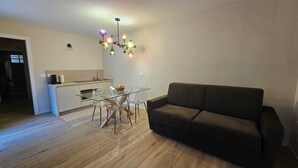 A modern living room with a glass dining table, a brown sofa, and a kitchen area with a white countertop and a hanging light fixture. - Relax and Comfort in an Elegant Venetian Villa with a Beautiful Outdoor Pool (Tregnago)