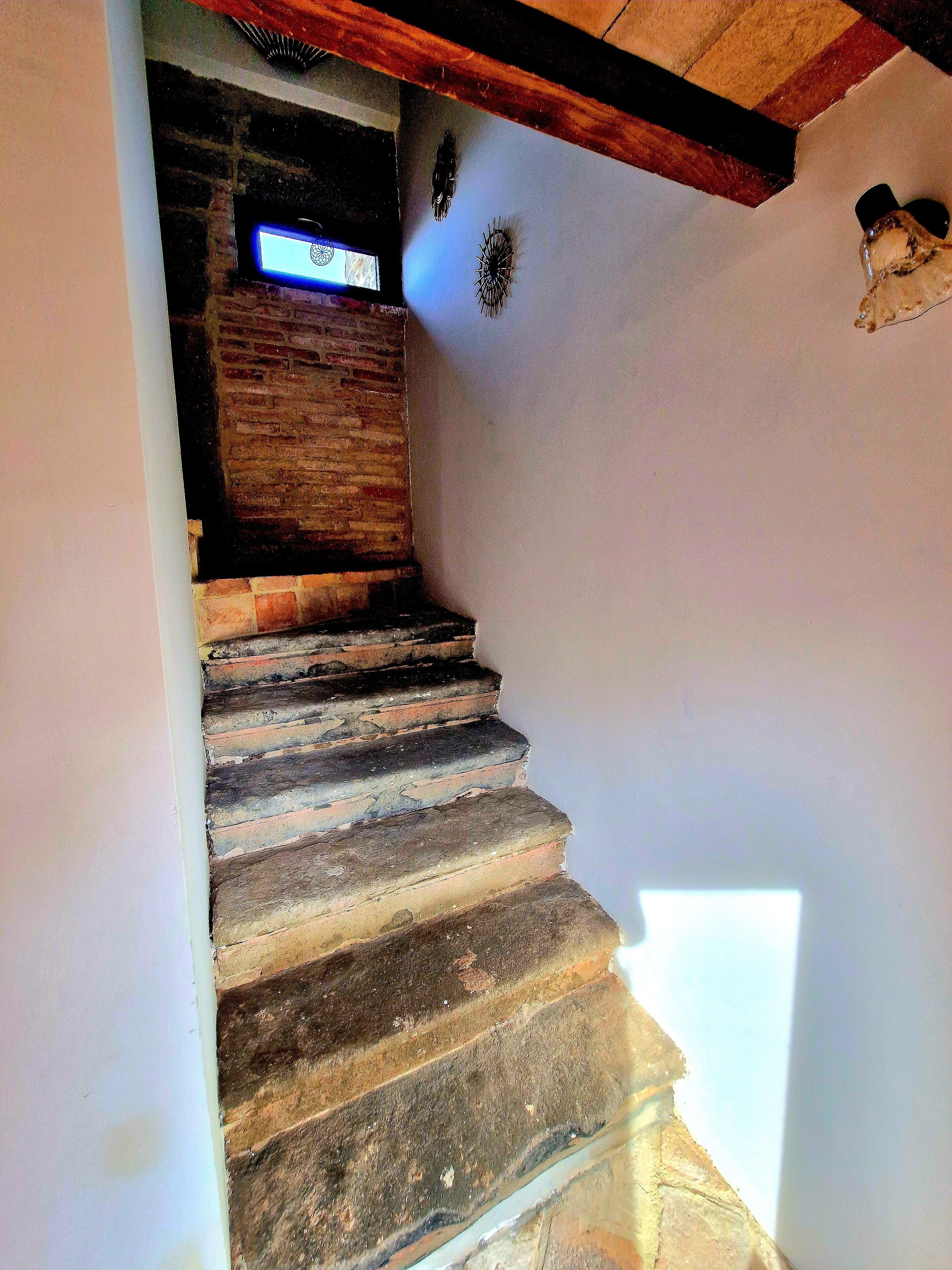 A stone staircase with a wooden beam ceiling, a brick wall, and a small window.