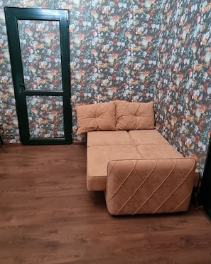 A room with a brown sofa, a floral wallpaper, and a wooden floor.