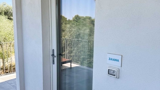 A door with a glass panel, a nameplate reading 'ZAIANA,' and a small electronic device on the wall.