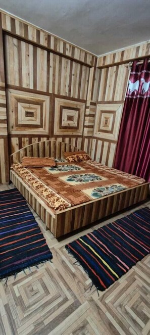 A bedroom with a wooden headboard, a bed with a floral bedspread, and two striped rugs on the floor.