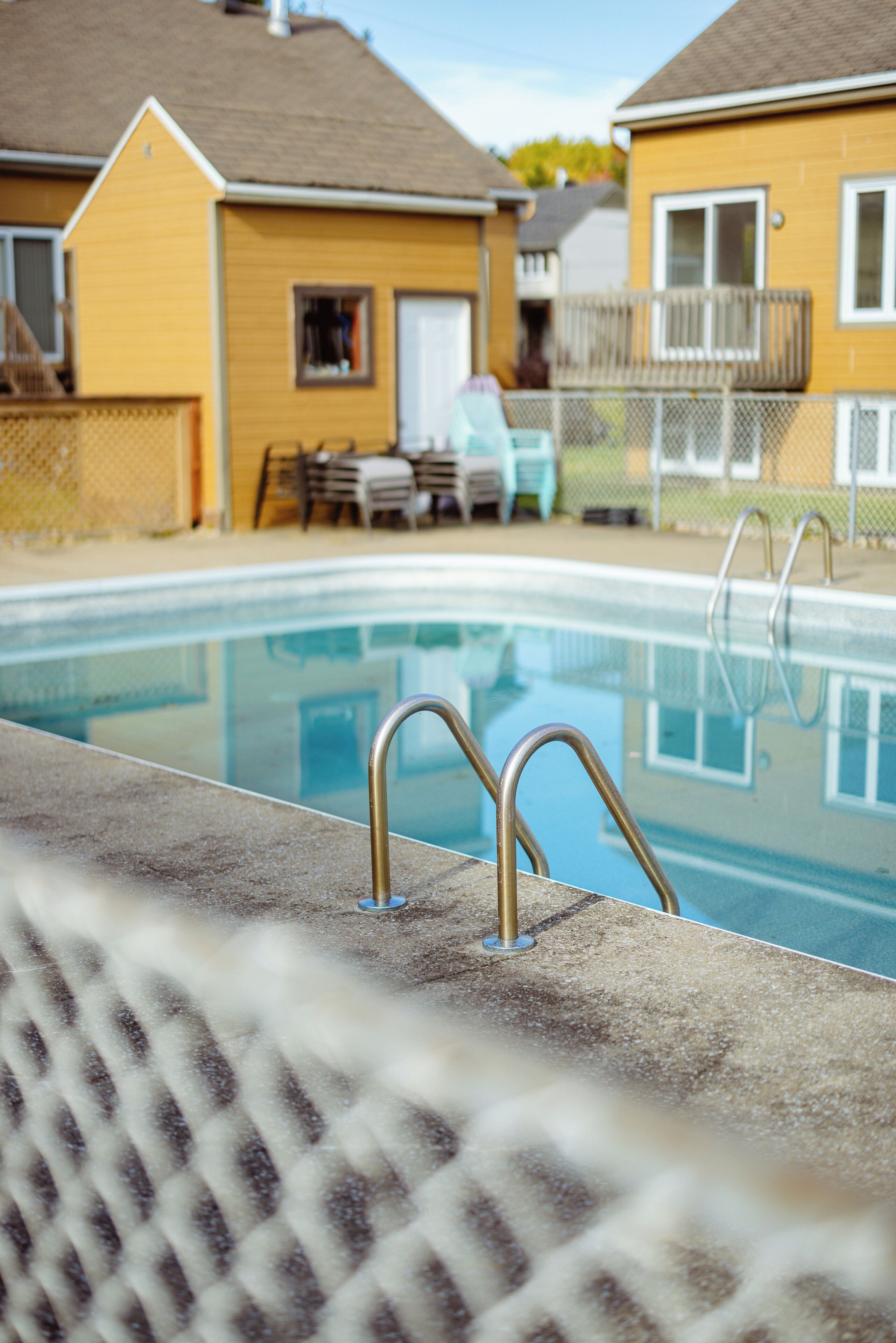 A swimming pool with metal ladders, surrounded by a fence, with houses in the background.