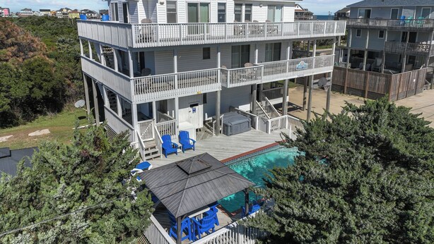 Una casa frente a la playa de dos pisos con balcón, piscina y mobiliario exterior.