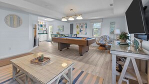 Amplia sala de estar con mesa de billar, mesa de comedor con centro de mesa de piña y un sillón cómodo.
