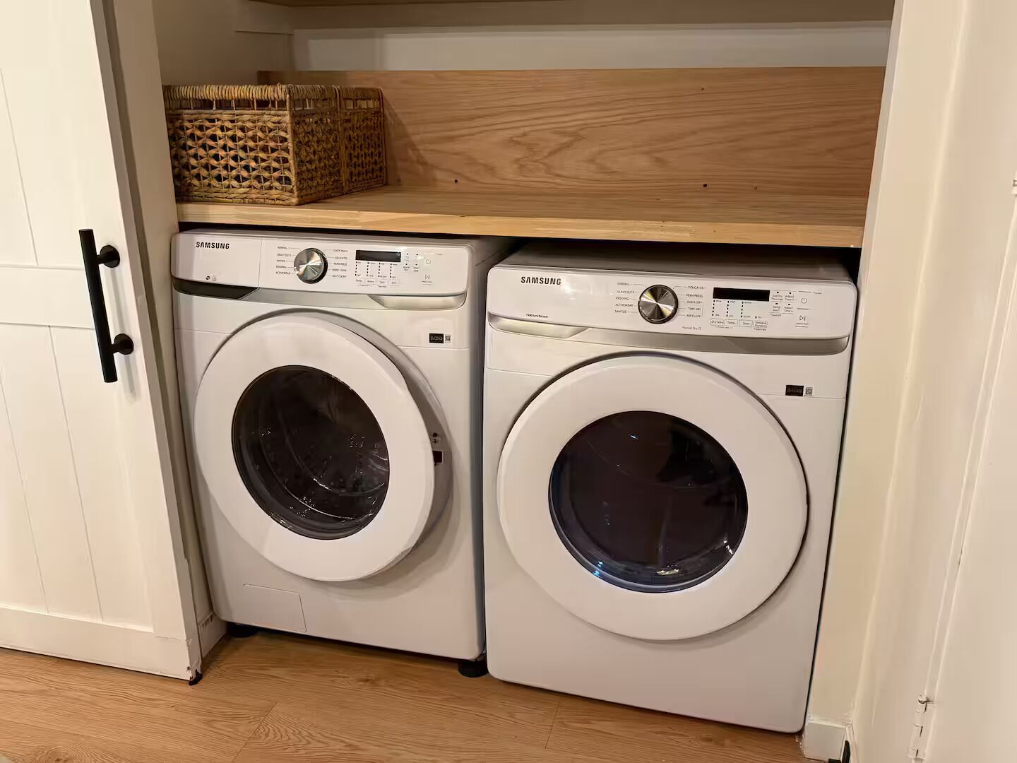 Deux machines à laver à chargement frontal, de couleur blanche, se trouvent dans une buanderie, avec une étagère en bois au-dessus.