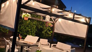 An outdoor patio area with a table and chairs, a pergola with string lights, and hanging plants.