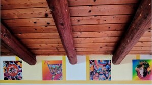 A wooden ceiling with exposed beams, a row of colorful paintings on the wall, and a double door at the bottom.