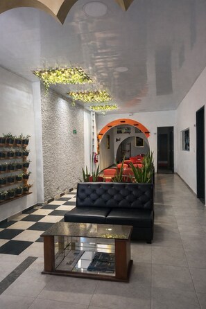 A lobby with a checkered floor, a glass-top coffee table, a black sofa, and a wall-mounted plant shelf. - Hotel Boutique La Trinidad (Neiva)