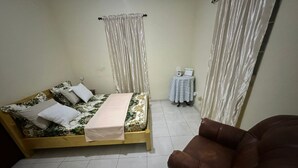 Une chambre à coucher avec un lit, une petite table, une chaise et des rideaux.