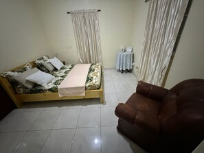 Ein Schlafzimmer mit einem Bett, einem kleinen Tisch, einem Sessel und Vorhängen.