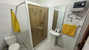 Une salle de bain comprenant des toilettes, un espace douche, un lavabo et un miroir.