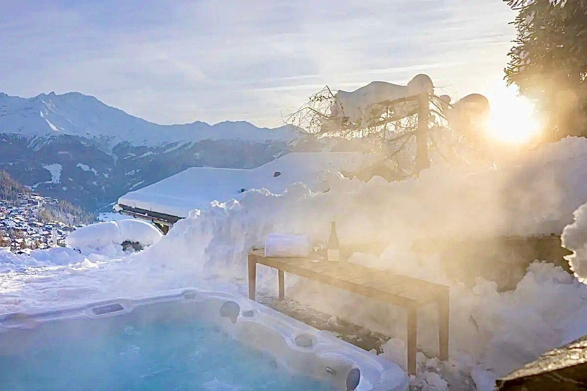 A hot tub surrounded by snow with mountains in the background.