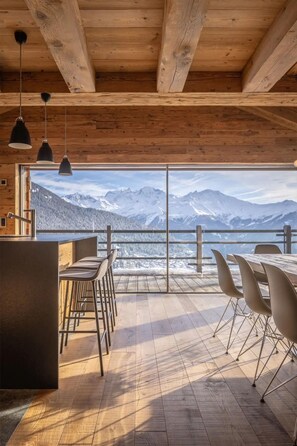 Un intérieur en bois avec une grande fenêtre donnant sur un paysage montagneux enneigé.