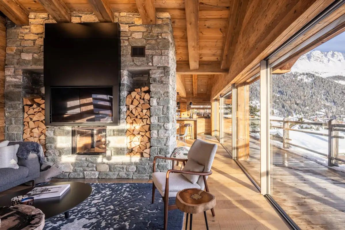 Un salon chaleureux avec une cheminée en pierre, un téléviseur à écran plat et une vue sur des montagnes enneigées.