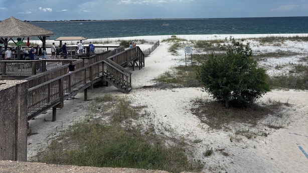 A beach with a wooden boardwalk, a thatched-roof structure, and a sandy area with sparse vegetation. - New 2BR Home in Perdido Key; Pet-Friendly Fenced Yard; Near Beach & Florabama (Pensacola)