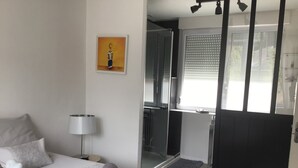 Una camera d'albergo con un letto, una doccia, una finestra con persiane e un quadro appeso al muro.