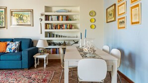 Un soggiorno con un divano blu, un tavolo bianco e una libreria piena di libri e oggetti decorativi.