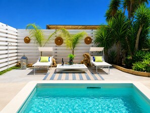 Un espace aménagé au bord de la piscine, comprenant deux chaises longues, une table et un mur décoratif orné d’éléments circulaires.