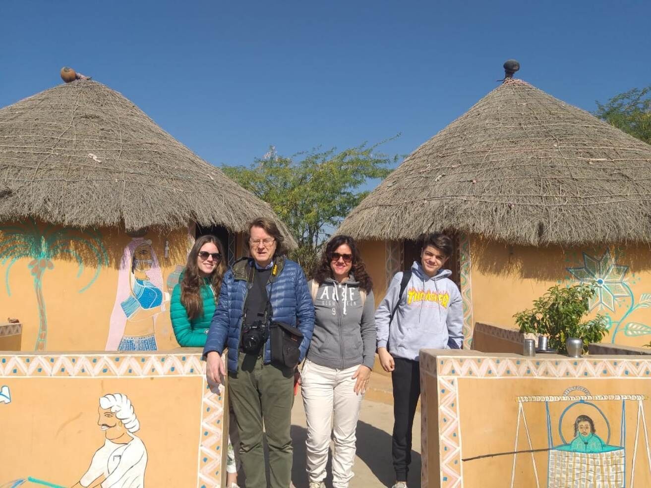 A group of people standing in front of a building with thatched roofs and a mural.