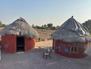 Two thatched-roof huts with red walls and a chair in front.