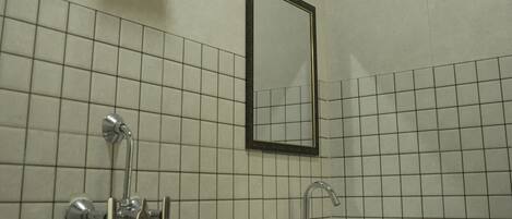 Une salle de bain avec un lavabo blanc, un miroir et une pomme de douche.