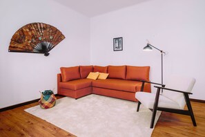 Una habitación de esquina con sofá seccional, una lámpara de pie, un ventilador y una mesita.