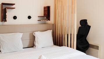 A hotel room with a bed, pillows, a towel, a chair, and a wall-mounted shelf.