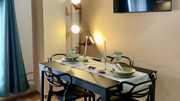 A dining table set with candles, glasses, and plates, with a mirror and lights above it. - 2bedrooms Apartment (4 pax) Residence Matteotti Novara  (NOVARA)