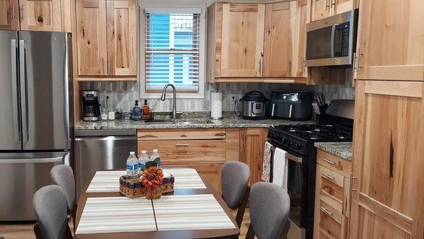 Una cucina moderna con mobili in legno, elettrodomestici in acciaio inossidabile e un'area pranzo con un tavolo apparecchiato per due.