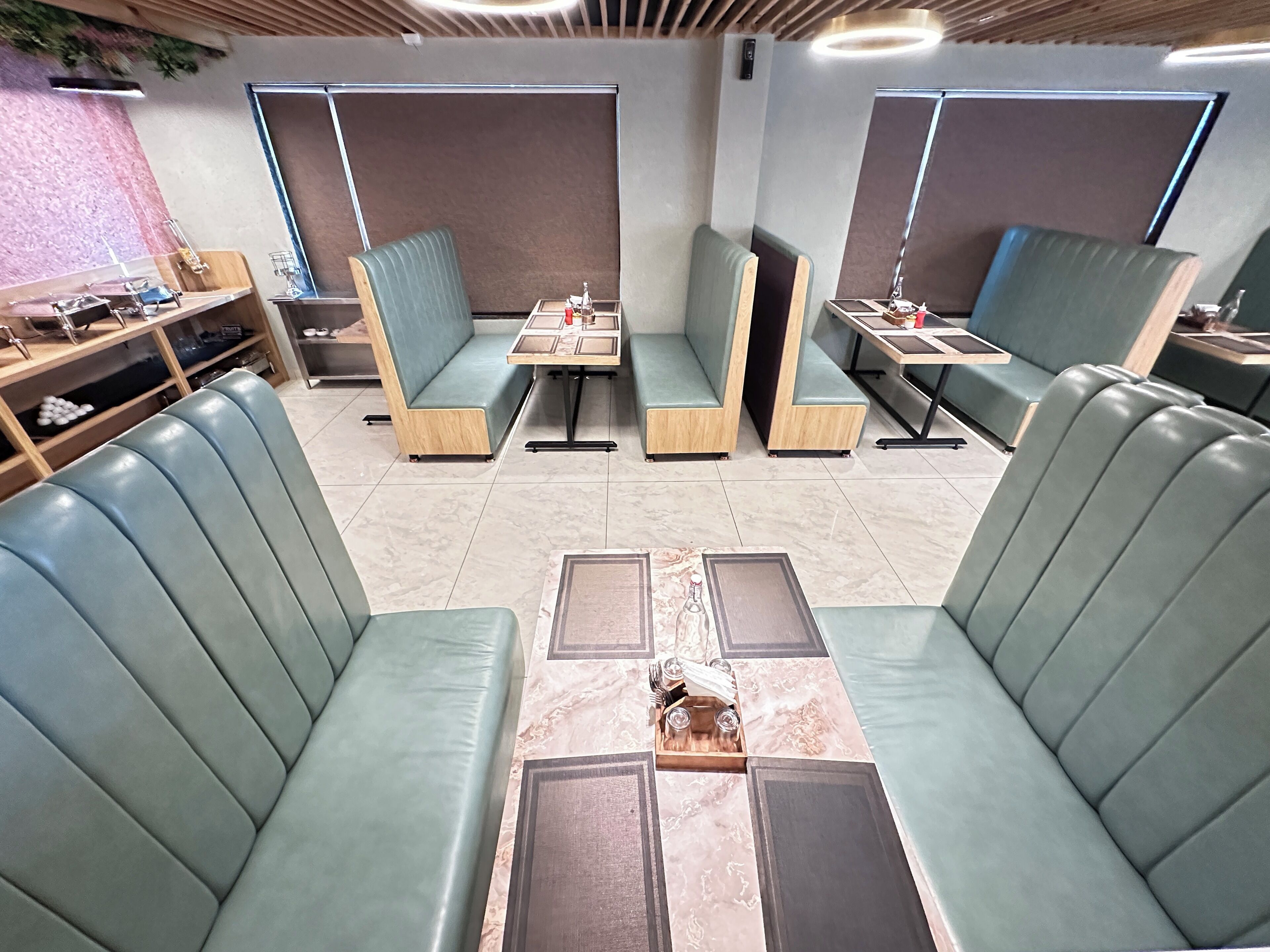 Un ristorante moderno con banquette e tavoli rivestiti di verde, caratterizzato da un design pulito e contemporaneo.