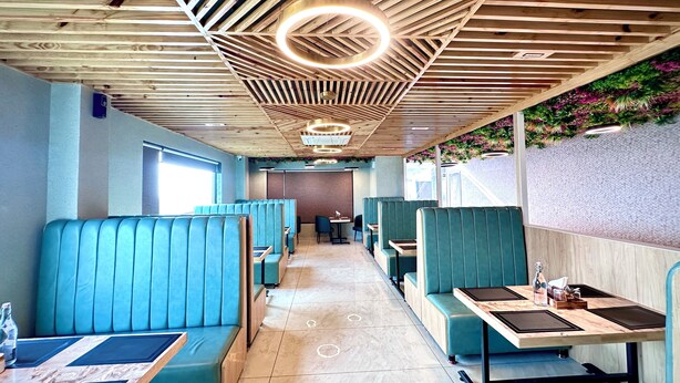 A restaurant interior with wooden ceiling beams, blue booths, and a long counter. - Hotel The Crown Inn Jhunjhunu (Jhunjhunu)