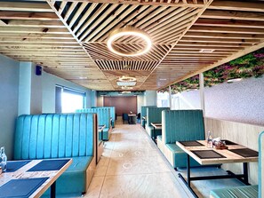 A restaurant interior with wooden ceiling beams, blue booths, and a long counter. - Hotel The Crown Inn Jhunjhunu (Jhunjhunu)