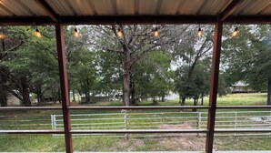 A covered outdoor area with a view of a fenced pasture and trees.