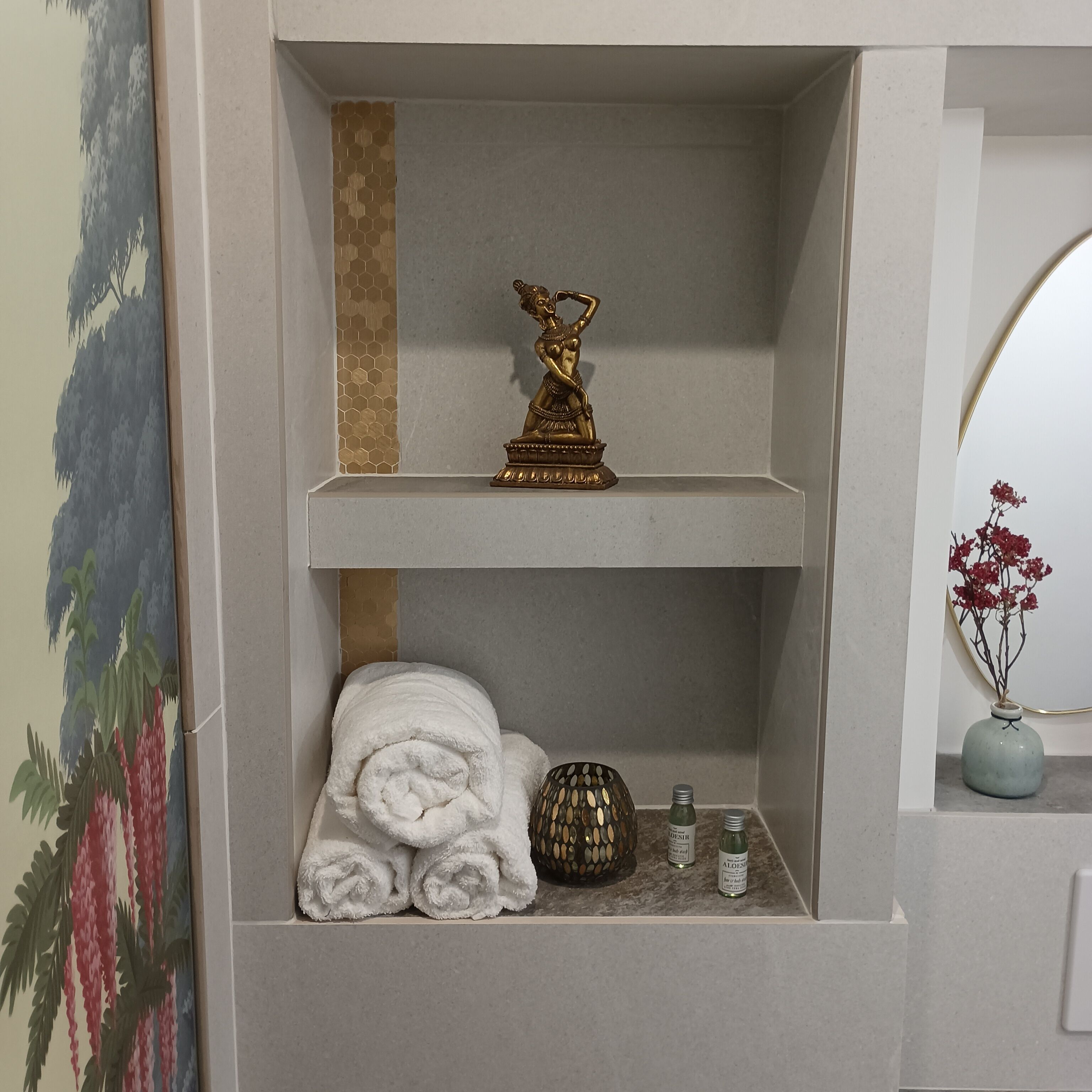 Une étagère de salle de bain avec une statuette dorée, des serviettes roulées et des articles de toilette.