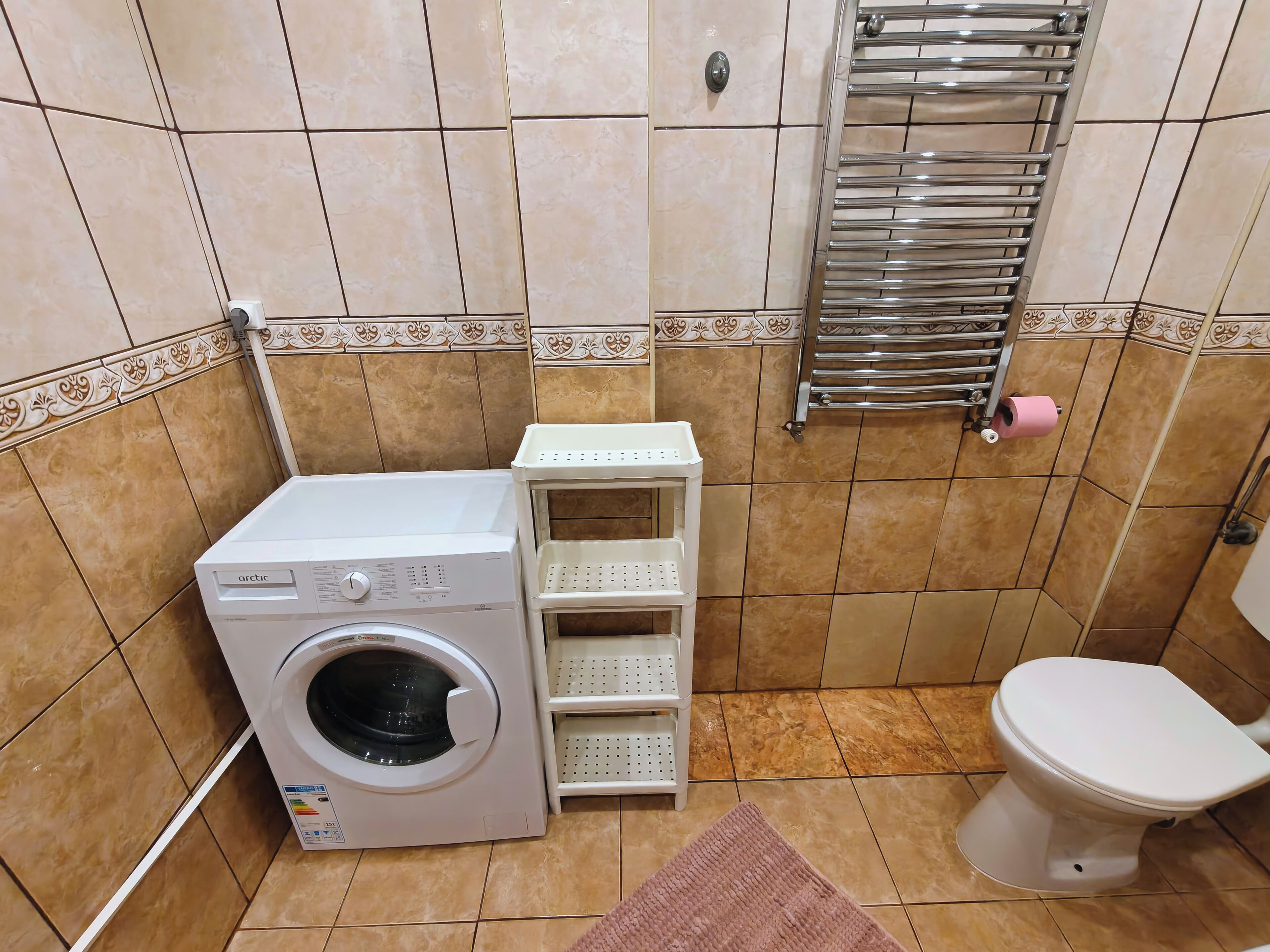 Een praktische badkamer met een wasmachine, toilet en handdoekhouder.