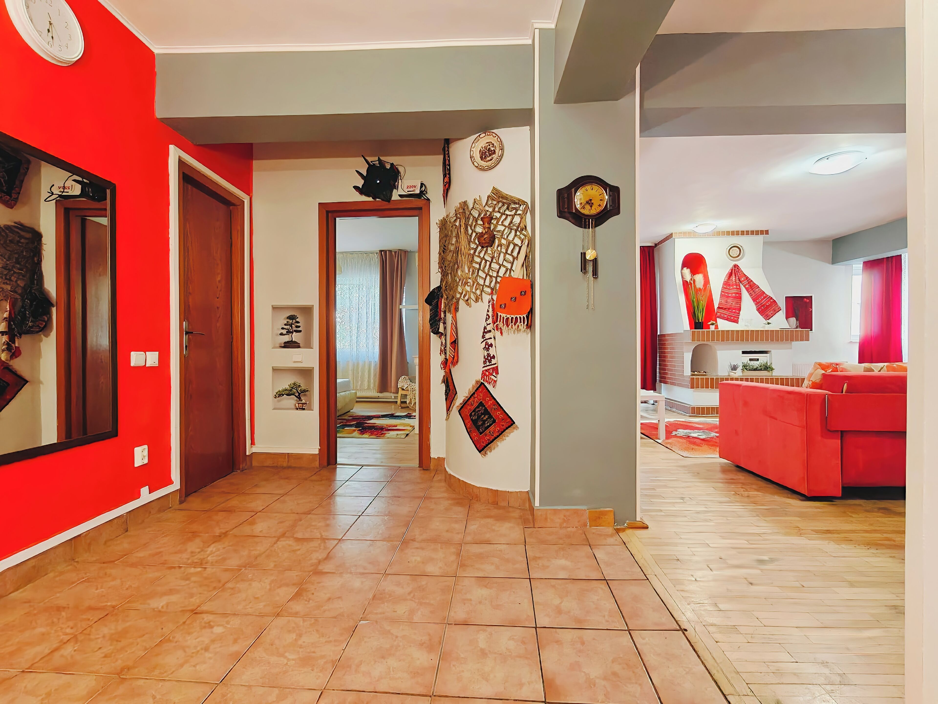 Un salón espacioso con un sofá rojo, suelo de madera y un pasillo que lleva a un dormitorio.