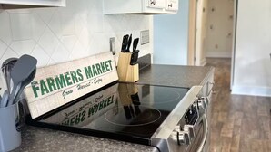Une cuisine équipée d’une hotte en acier inoxydable, d’une planche à découper en bois portant l’inscription « Marché de producteurs » et d’un bloc à couteaux.