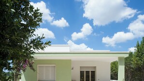A building with a covered patio area, two windows with shutters, and a seating arrangement with two chairs and a small table. - VILLIN0 DEI PINI - Relaxation in Salento (Puglia)