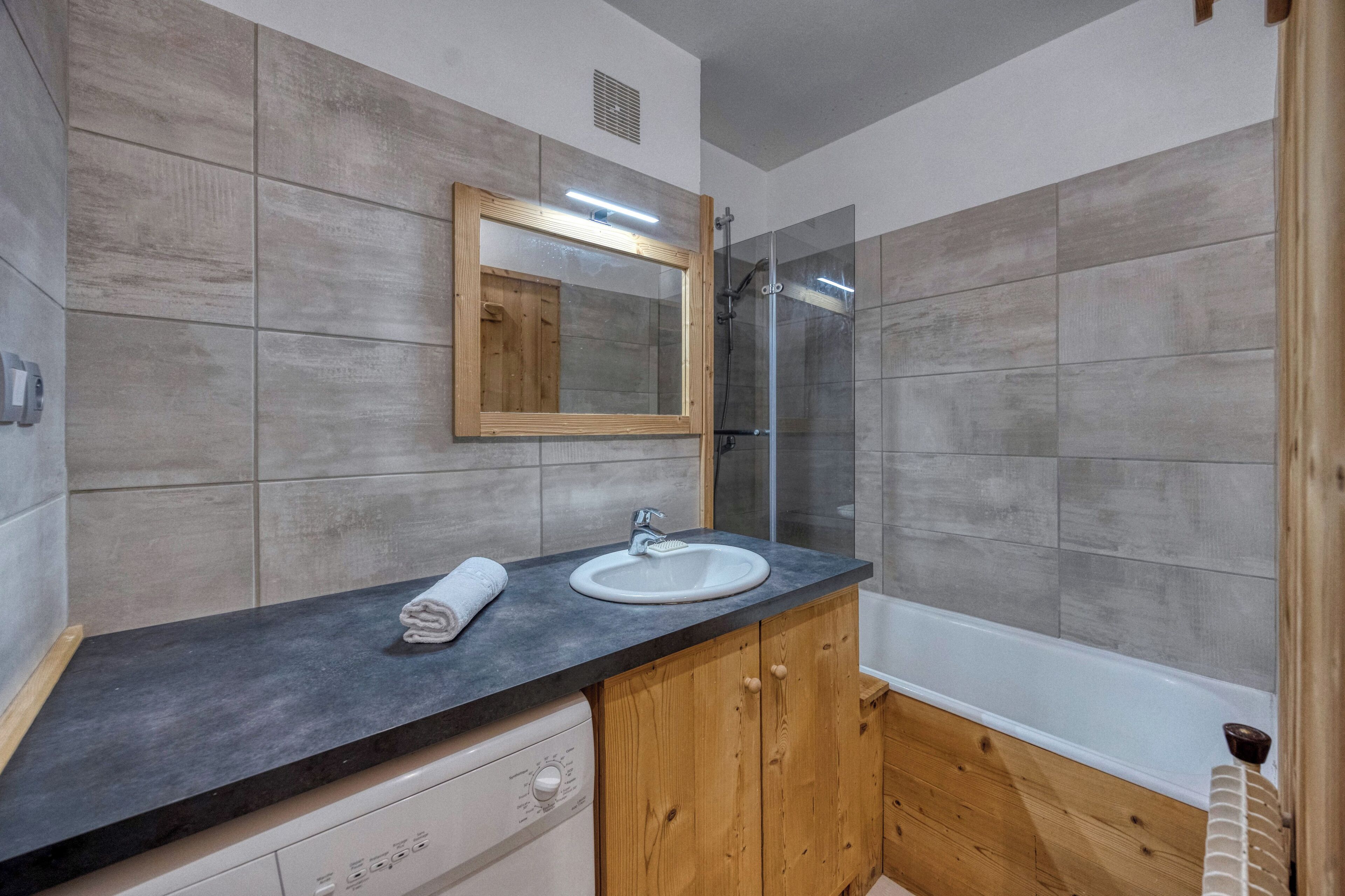 A bathroom with a wooden vanity, a white sink, and a glass shower enclosure.