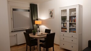 Un comedor con una mesa, sillas, una lámpara y un aparador con libros y juegos.