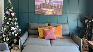 Een moderne woonkamer met een grijze bank, een stadslandschap schilderij, een versierde kerstboom en teal muren.