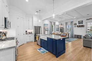 A modern kitchen with white cabinets, a blue island, stainless steel appliances, and a dining area with a view of the city.