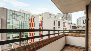 En balkong med en tegelbeklädd avsats och ett metallräcke, med utsikt över en stadsbild med moderna byggnader.