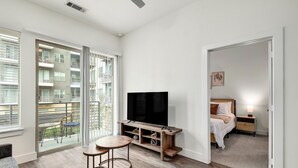 Una habitación de hotel moderna con un televisor grande, un balcón con mobiliario exterior y una zona de estar acogedora.