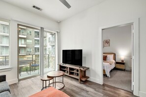 A modern hotel room with a large TV, a balcony with outdoor furniture, and a cozy seating area. - Modern 1-bedroom apartment in Alamo City Loft • Downtown • Riverwalk (San Antonio)