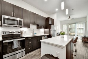 A modern kitchen with dark wood cabinets, stainless steel appliances, and a white countertop. - Modern 1-bedroom apartment in Alamo City Loft • Downtown • Riverwalk (San Antonio)