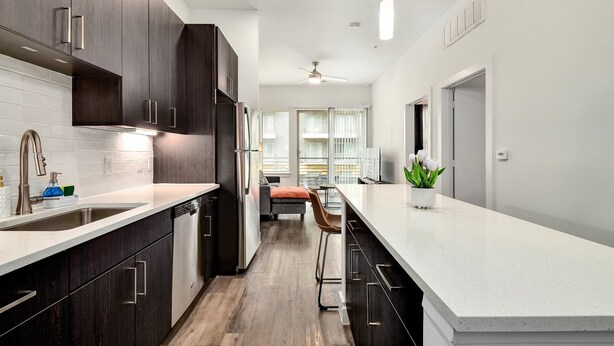Una cocina moderna con armarios de madera oscura, encimera blanca y una zona de bar.
