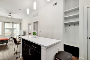 A modern kitchen with a white countertop, black cabinets, and a small island. There is a dining area with a table and chairs, and a large window providing natural light. - Modern 1-bedroom apartment in Alamo City Loft • Downtown • Riverwalk (San Antonio)