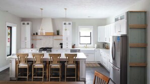 Une cuisine moderne avec des meubles blancs, un îlot central doté de tabourets, des appareils en acier inoxydable et un éclairage suspendu.