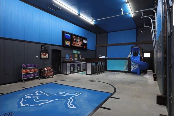 Uma pista de boliche com piso azul, balcão e tela exibindo jogos de boliche.